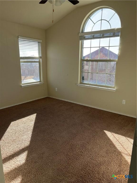 unfurnished room featuring vaulted ceiling, dark carpet, a ceiling fan, and baseboards