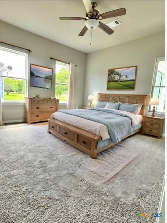 carpeted bedroom with a ceiling fan, multiple windows, and visible vents