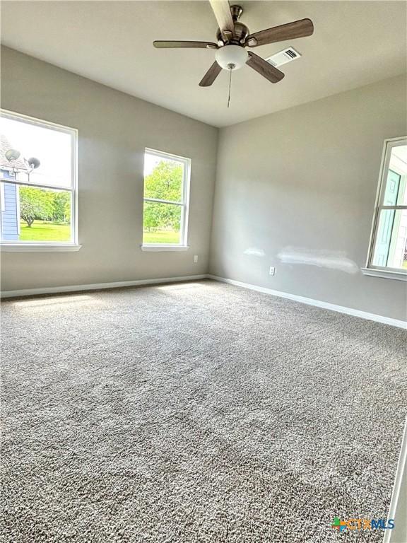 carpeted empty room with a healthy amount of sunlight, a ceiling fan, visible vents, and baseboards