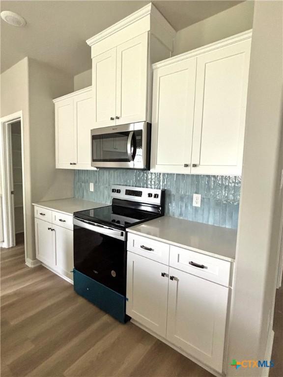 kitchen with white cabinets, light wood-style floors, stainless steel appliances, light countertops, and backsplash
