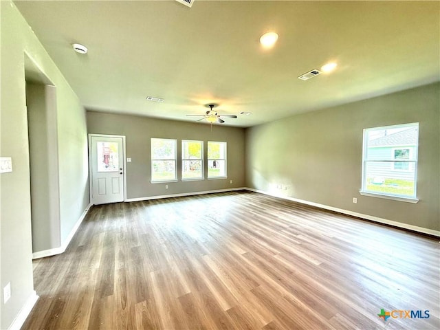 unfurnished living room with wood finished floors, visible vents, ceiling fan, and baseboards