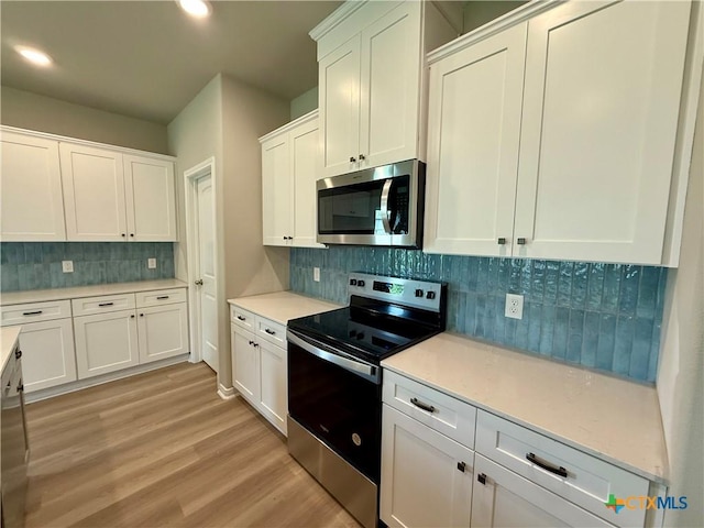 kitchen with tasteful backsplash, white cabinets, appliances with stainless steel finishes, light wood-style floors, and light countertops