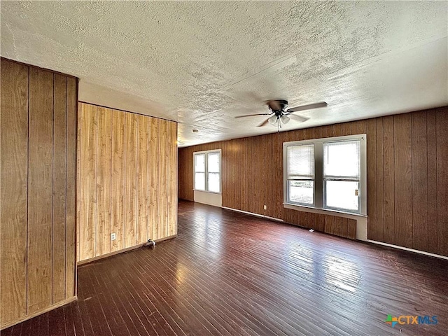 empty room featuring wood walls, ceiling fan, a textured ceiling, and dark wood-style flooring