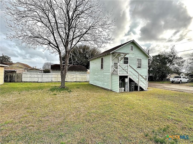 rear view of property with stairs, a lawn, and fence