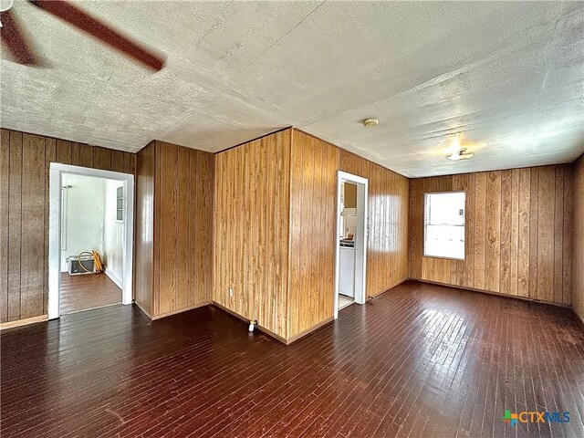 unfurnished room with a textured ceiling, wood walls, and dark wood finished floors