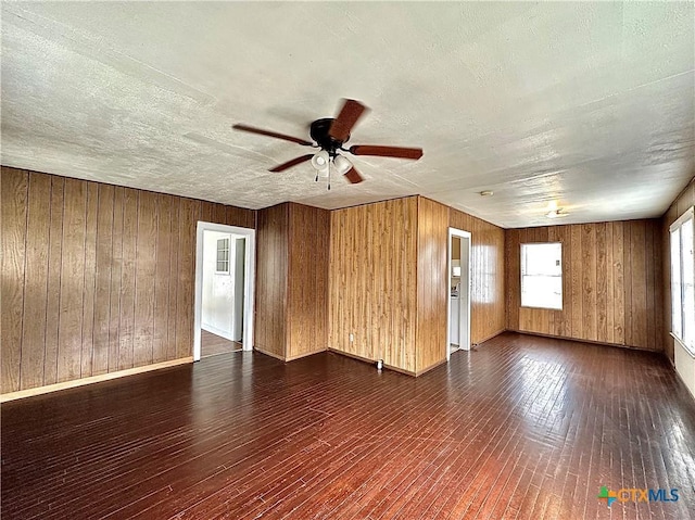 unfurnished room featuring dark wood-style floors, a textured ceiling, a ceiling fan, and wooden walls