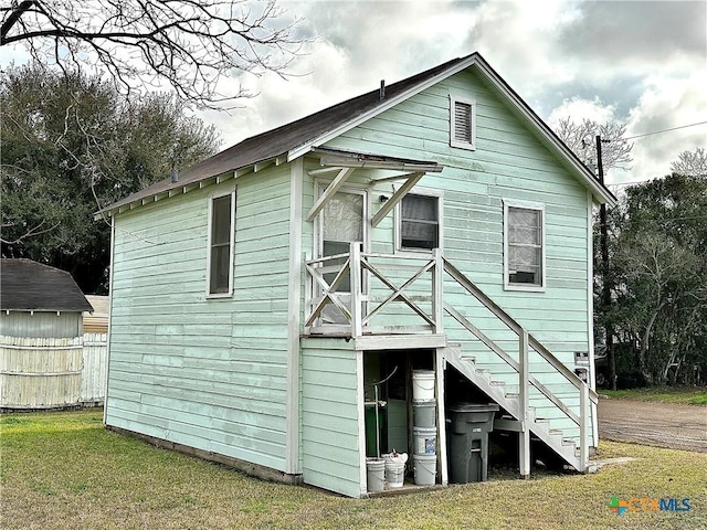 rear view of property featuring a yard, an outdoor structure, and fence