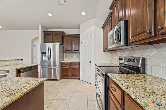 519 Gianotti Ct, Temple, TX 76502 - kitchen featuring stainless steel appliances, backsplash, arched walkways, light stone counters, and light tile patterned floors