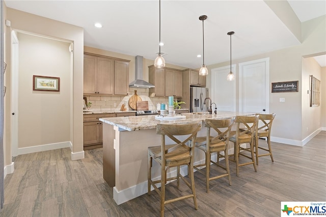 kitchen featuring wood-type flooring, a kitchen island with sink, wall chimney exhaust hood, and stainless steel appliances