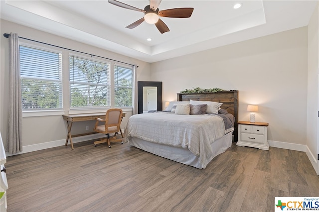 bedroom with hardwood / wood-style flooring, ceiling fan, and a raised ceiling