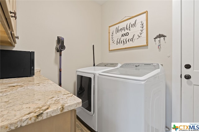 clothes washing area with light wood-type flooring, washer and clothes dryer, and cabinets