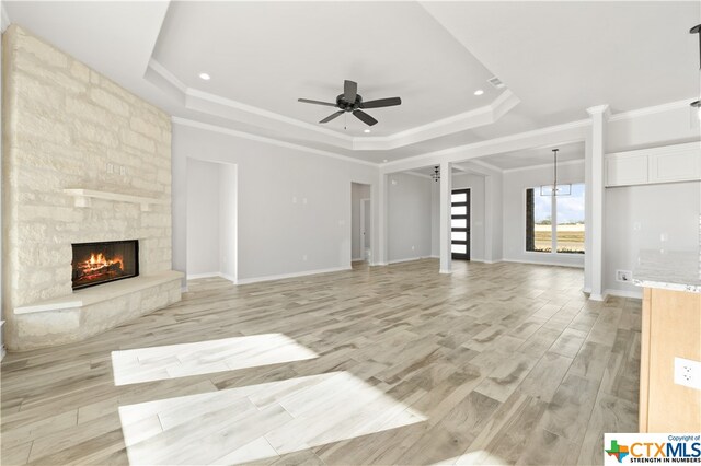 unfurnished living room featuring ceiling fan with notable chandelier, a tray ceiling, a fireplace, crown molding, and light wood-type flooring