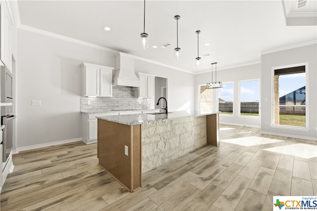 kitchen with white cabinets, premium range hood, a large island with sink, and light hardwood / wood-style flooring