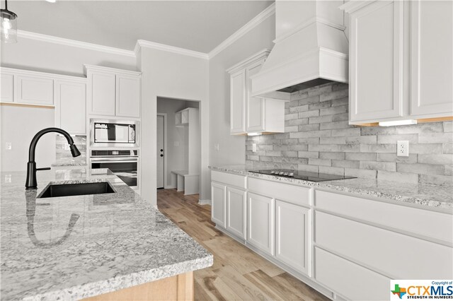 kitchen with stainless steel oven, light wood-type flooring, custom range hood, and white cabinets