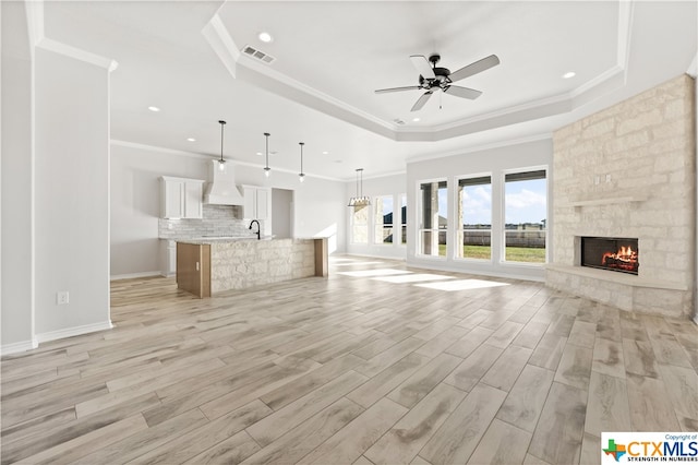 unfurnished living room featuring a fireplace, ceiling fan, a raised ceiling, and light wood-type flooring