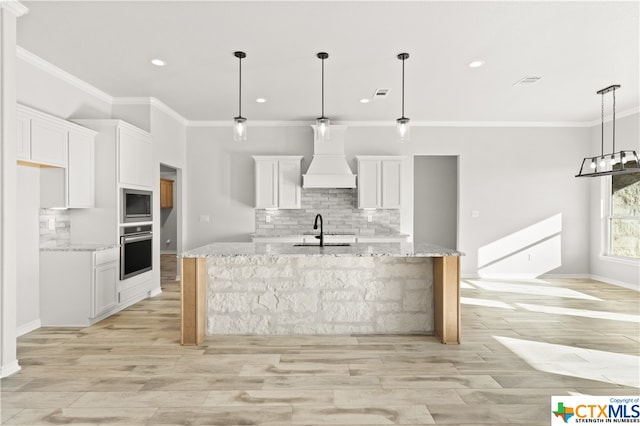 kitchen with white cabinetry, light stone counters, appliances with stainless steel finishes, custom exhaust hood, and decorative light fixtures