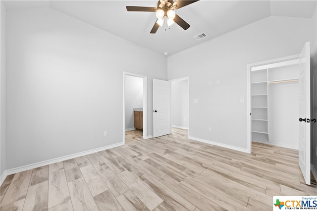 unfurnished bedroom with ceiling fan, a spacious closet, a closet, light wood-type flooring, and vaulted ceiling