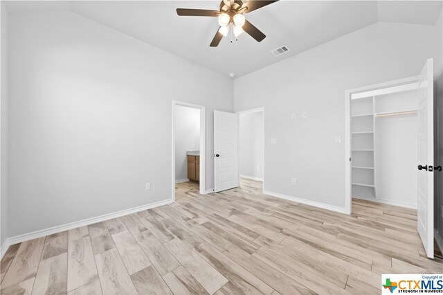 unfurnished bedroom with ceiling fan, a spacious closet, a closet, light wood-type flooring, and vaulted ceiling