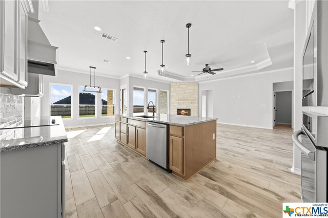 kitchen featuring stainless steel appliances, decorative light fixtures, a large island with sink, ceiling fan, and light hardwood / wood-style flooring