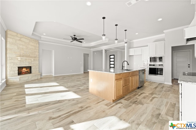 kitchen with light stone counters, stainless steel appliances, a large island, sink, and white cabinets