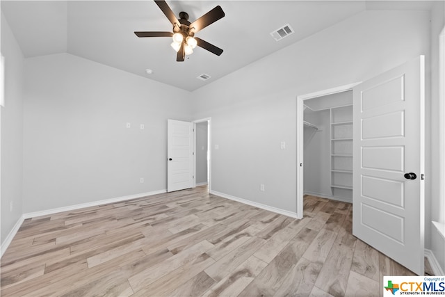 unfurnished bedroom with ceiling fan, light hardwood / wood-style flooring, lofted ceiling, a walk in closet, and a closet