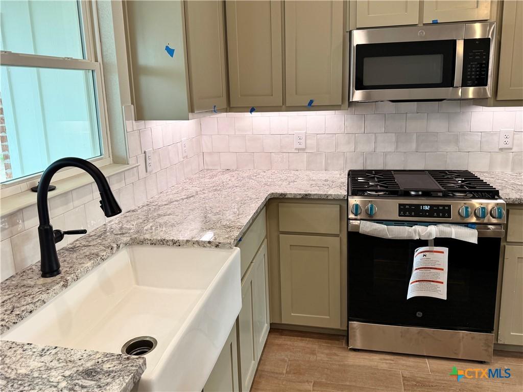 6018 Parma Ln, Temple, TX 76502 - kitchen featuring appliances with stainless steel finishes, a sink, light wood-type flooring, tasteful backsplash, and light stone countertops