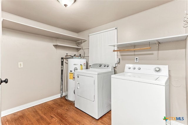 clothes washing area with electric water heater, laundry area, separate washer and dryer, baseboards, and light wood-type flooring