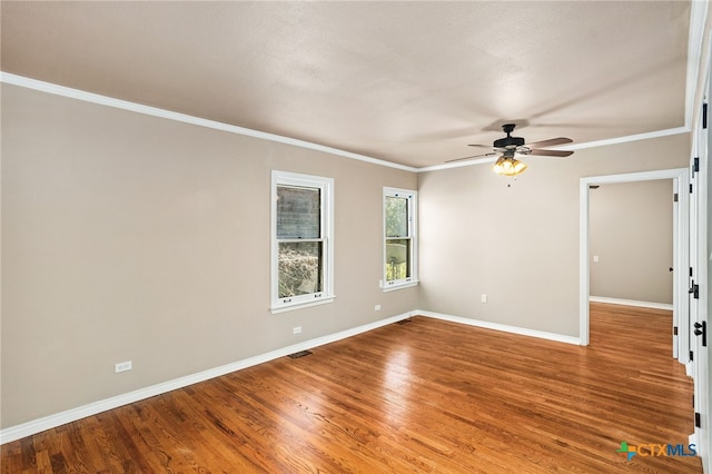 empty room with ornamental molding, wood finished floors, a ceiling fan, and baseboards