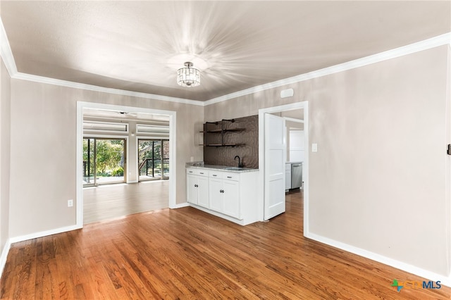 unfurnished living room featuring a sink, crown molding, baseboards, and wood finished floors