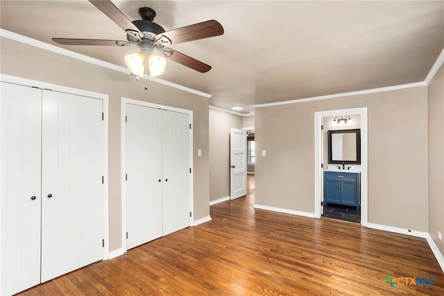 unfurnished bedroom featuring crown molding, baseboards, wood finished floors, and multiple closets