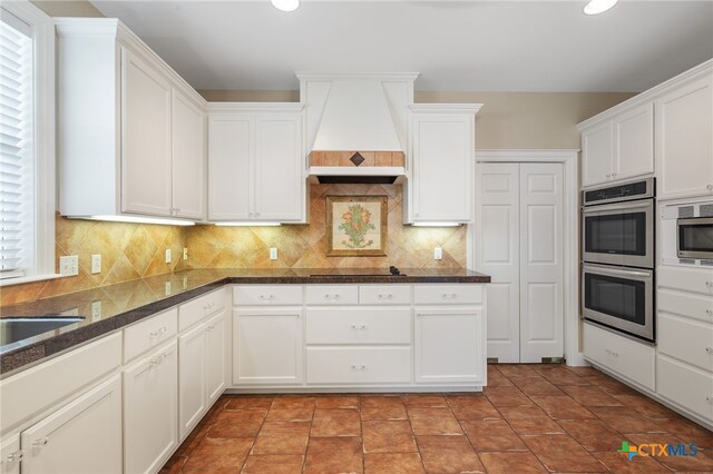 kitchen featuring tasteful backsplash, white cabinetry, appliances with stainless steel finishes, dark stone countertops, and custom exhaust hood