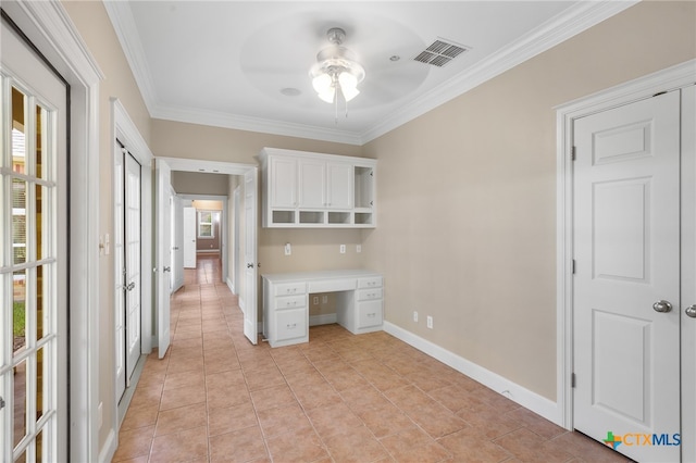 unfurnished office with light tile patterned floors, built in desk, ceiling fan, and crown molding