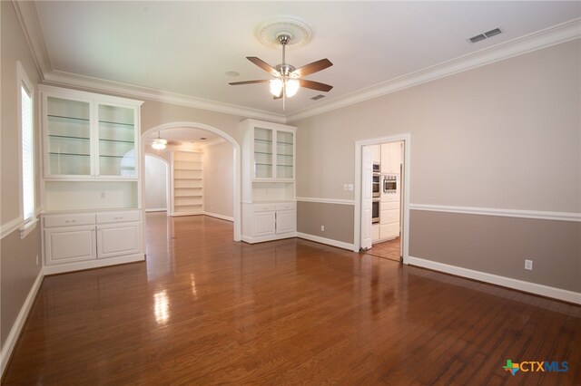 empty room featuring dark wood-type flooring, ceiling fan, built in features, and ornamental molding