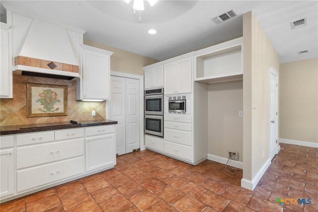 kitchen with stainless steel appliances, custom range hood, white cabinetry, and tasteful backsplash