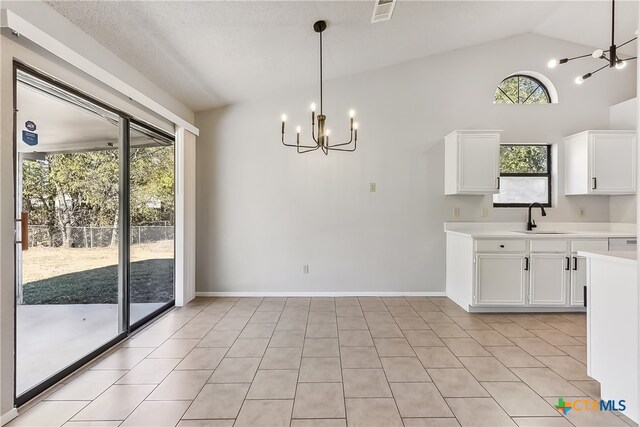 unfurnished dining area featuring sink, a chandelier, a textured ceiling, lofted ceiling, and light tile patterned floors