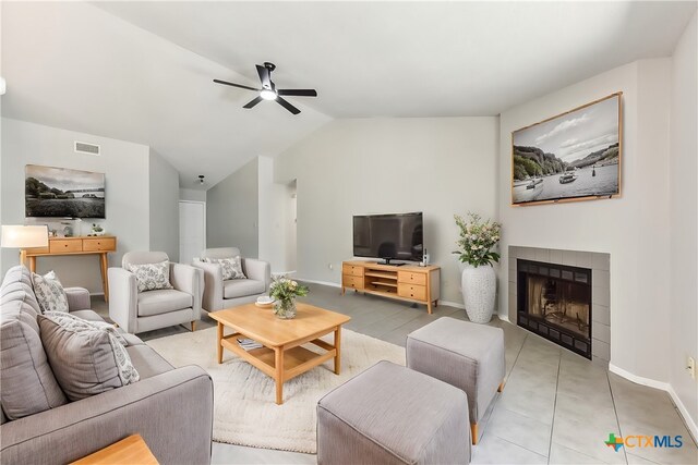 living room featuring a tile fireplace, light tile patterned floors, vaulted ceiling, and ceiling fan