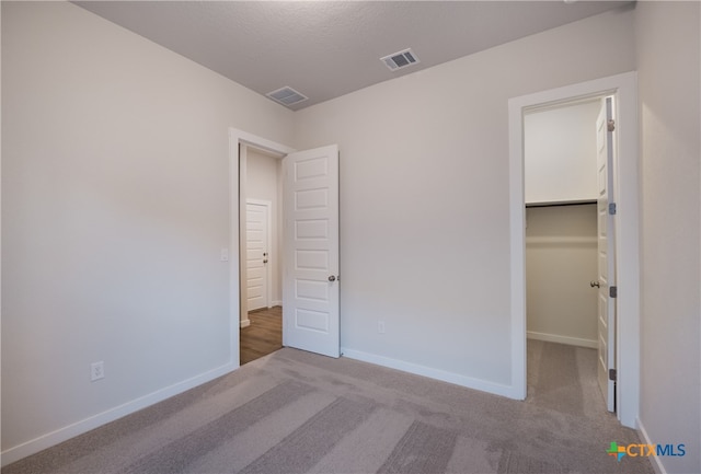 unfurnished bedroom featuring light colored carpet, a textured ceiling, a closet, and a spacious closet