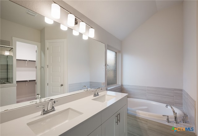 bathroom with vanity, lofted ceiling, and tiled tub