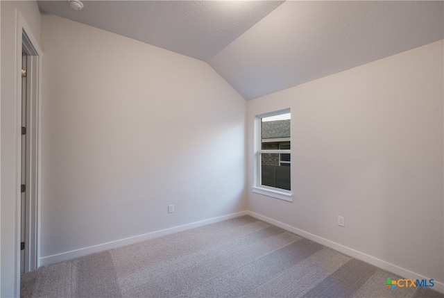 carpeted spare room with vaulted ceiling