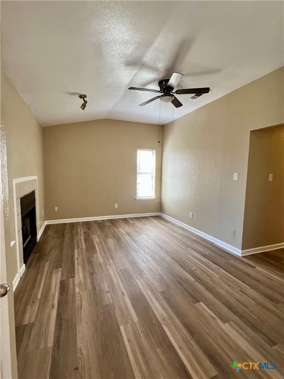 unfurnished living room with dark wood-type flooring, a tile fireplace, vaulted ceiling, and baseboards