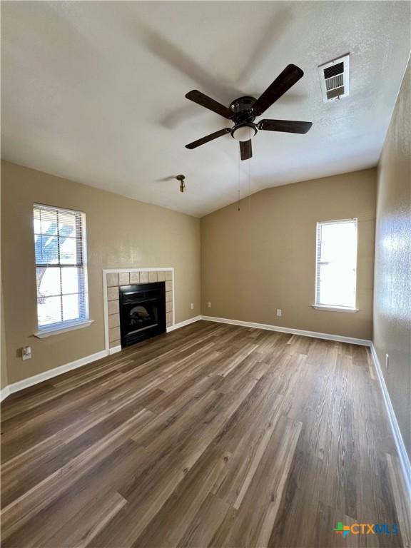 unfurnished living room featuring plenty of natural light, a fireplace, visible vents, and dark wood-type flooring