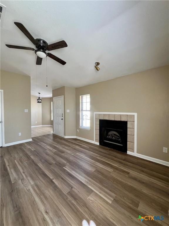 unfurnished living room with ceiling fan, a tile fireplace, wood finished floors, and baseboards