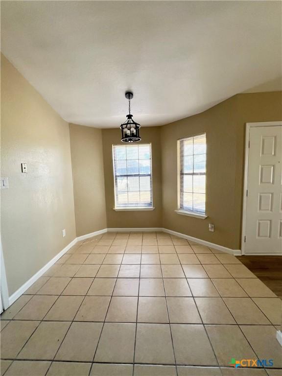 unfurnished dining area with an inviting chandelier, baseboards, and light tile patterned flooring