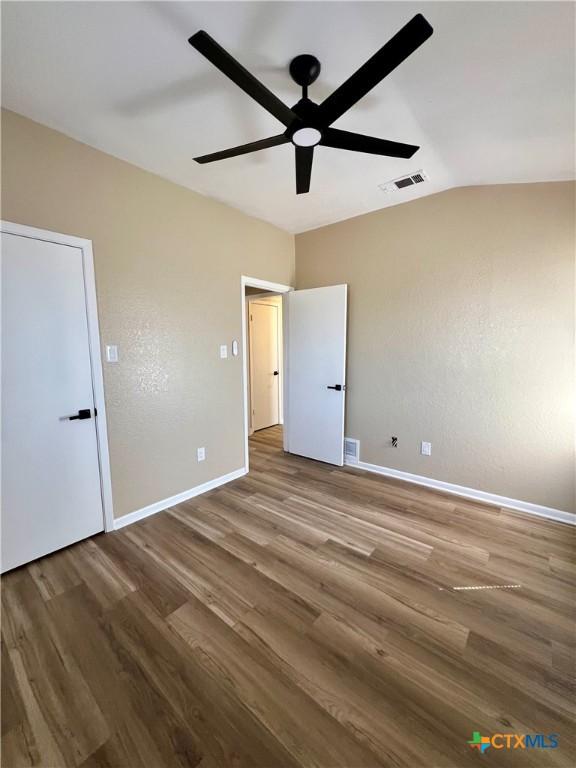 unfurnished bedroom with visible vents, baseboards, vaulted ceiling, and wood finished floors