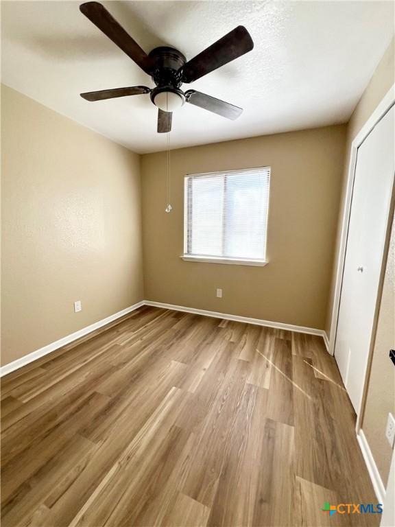 unfurnished bedroom featuring a closet, wood finished floors, a ceiling fan, and baseboards