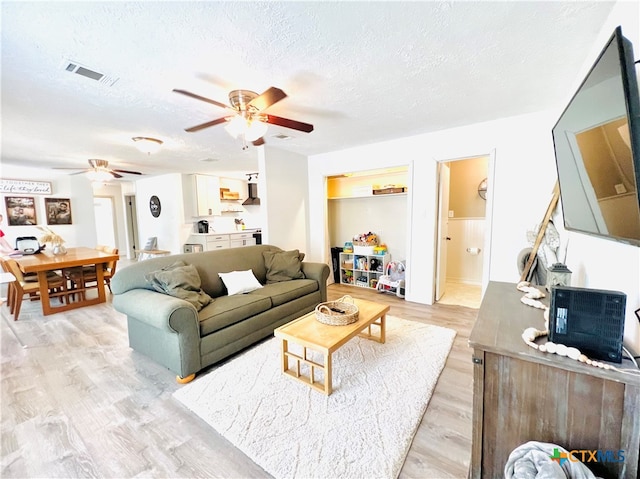 living room featuring light wood-type flooring, a textured ceiling, and ceiling fan