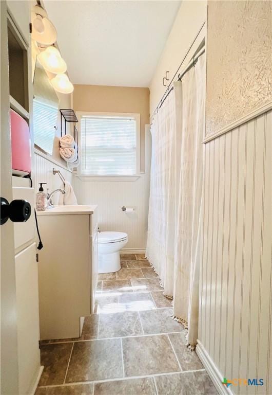 613 E 5th St, Cameron, TX 76520 - full bath featuring vanity, a wainscoted wall, stone finish floors, toilet, and curtained shower