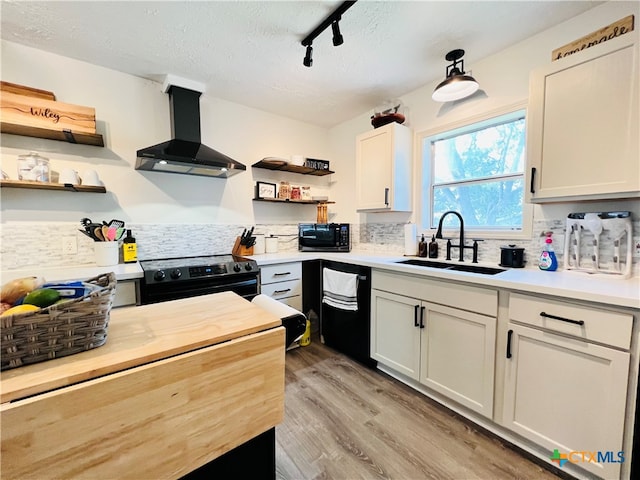 kitchen featuring sink, black appliances, range hood, white cabinets, and decorative backsplash