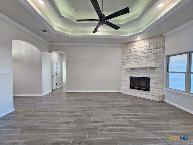 unfurnished living room with ceiling fan, wood-type flooring, a fireplace, ornamental molding, and a raised ceiling