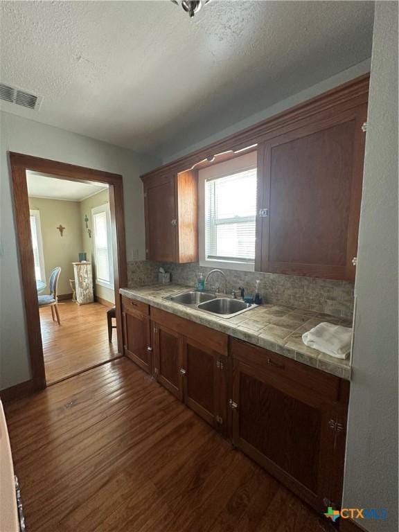 kitchen featuring visible vents, dark wood-style floors, tile counters, tasteful backsplash, and a sink